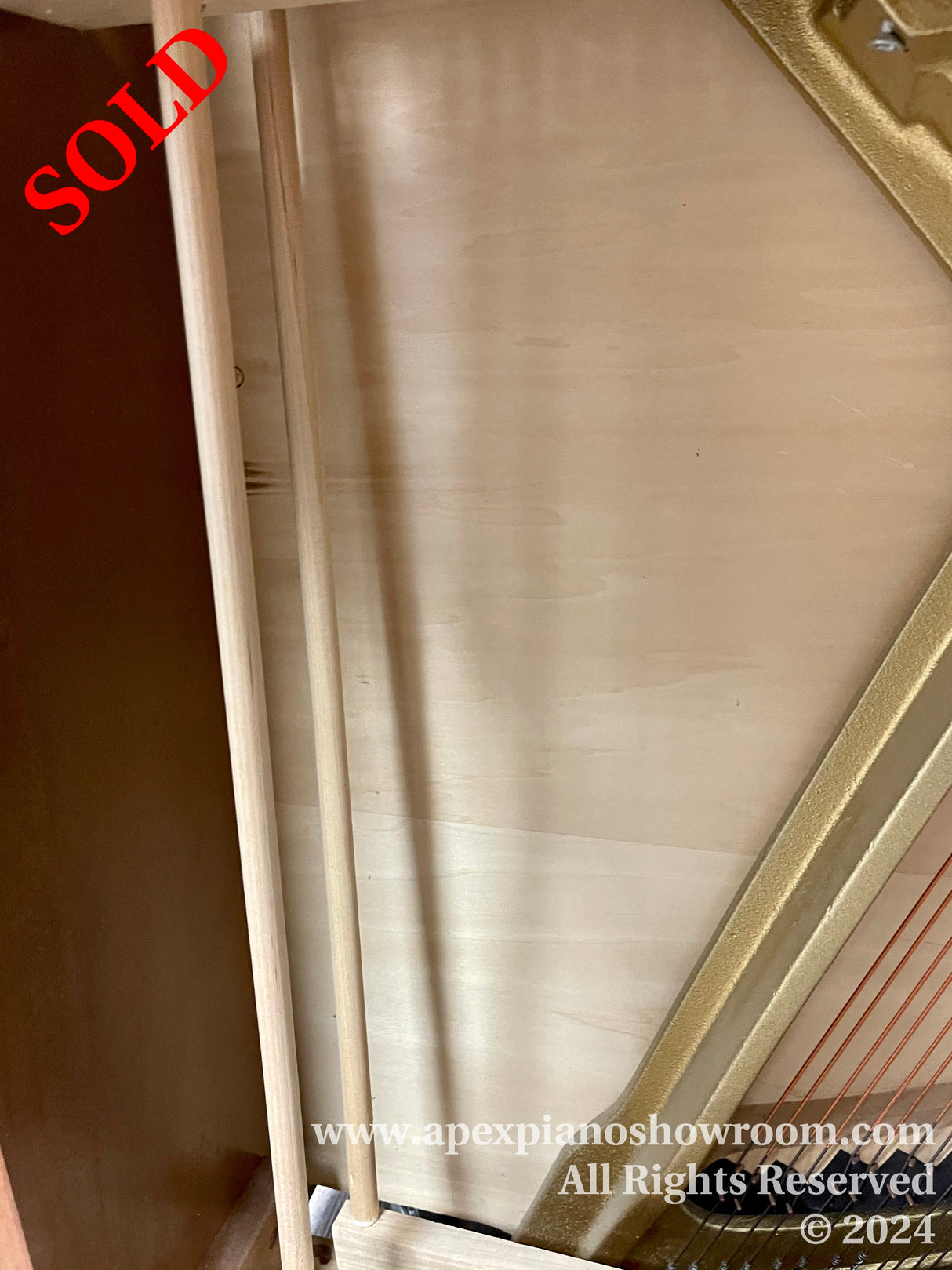 Close-up view of a grand piano's gold-painted cast iron plate, showing the strings and tuning pins, with a focus on the craftsmanship of the plate's interior.