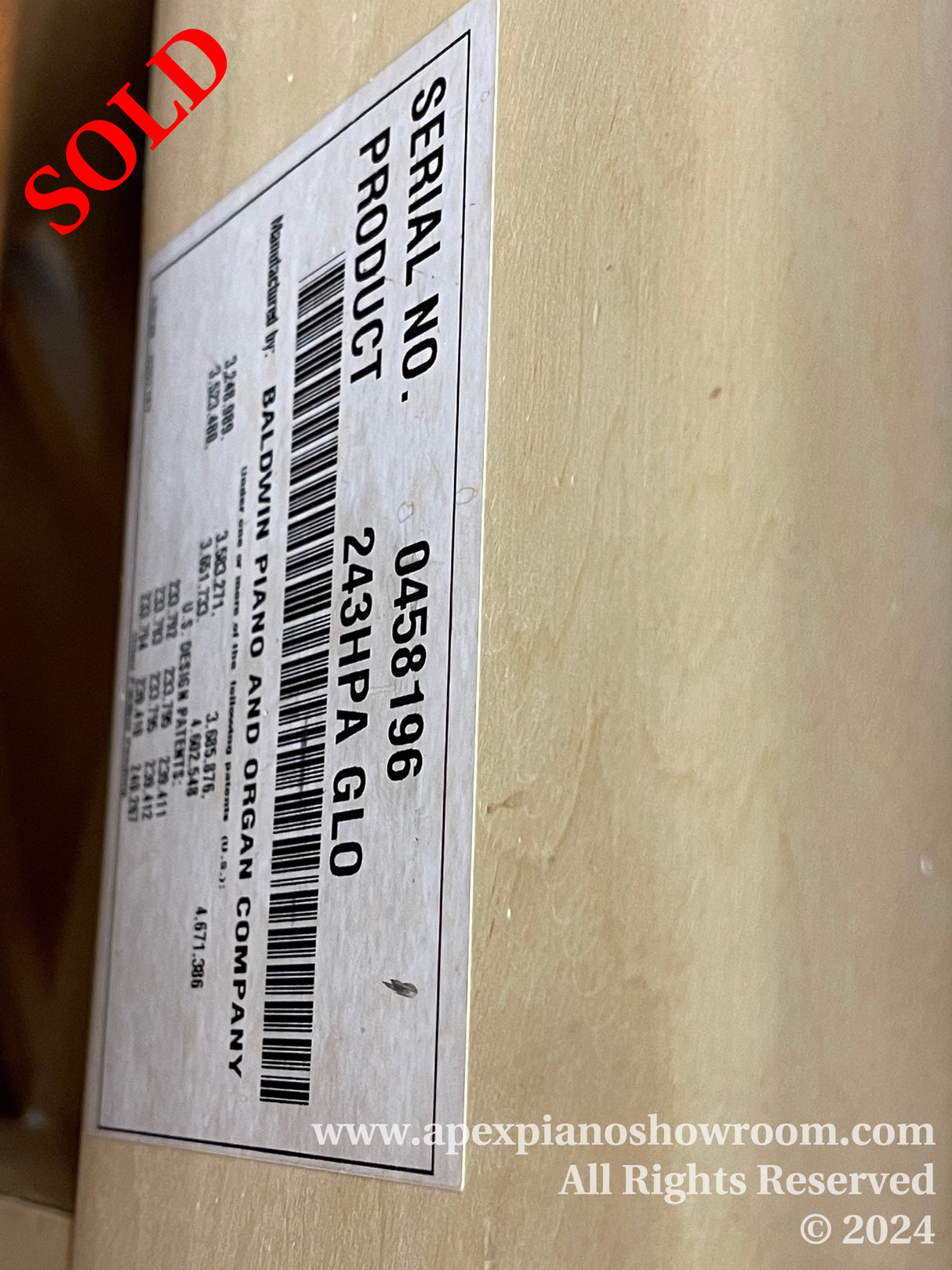 Close-up of a Baldwin pianos serial number sticker attached to the wood, indicating model and serial details for identification and tracking within the piano industry.