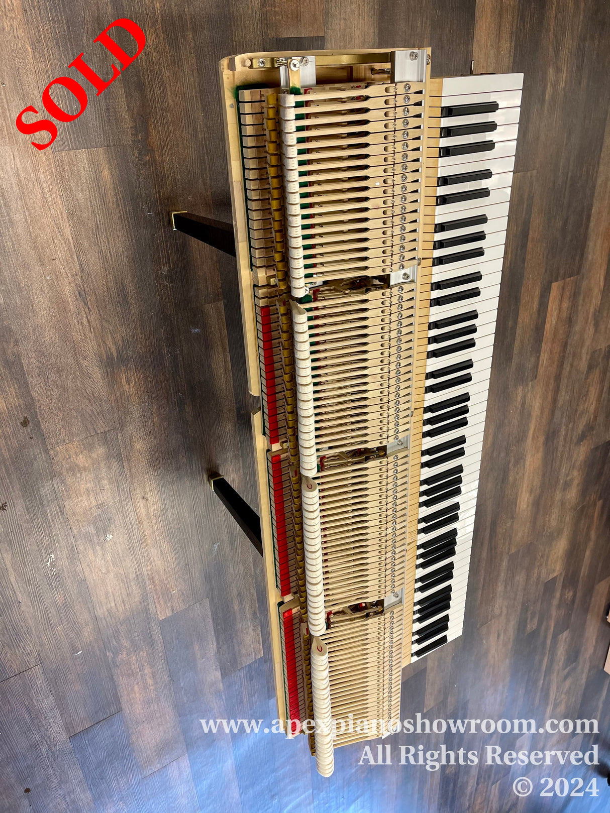 A disassembled upright piano showcasing its internal mechanism and keyboard, with hammers and strings visible, set against a wooden floor background.