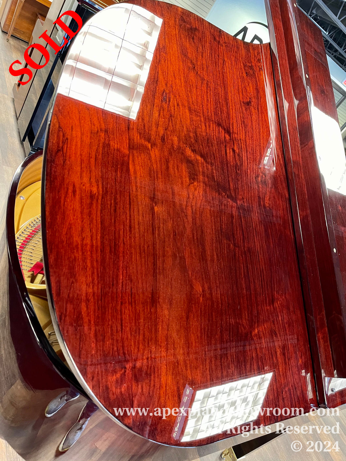 Close-up view of a grand piano showcasing its glossy, mahogany finish and the intricate wood patterns — part of the keyboard and the interior strings and hammers are also visible, highlighting the craftsmanship of the piano.
