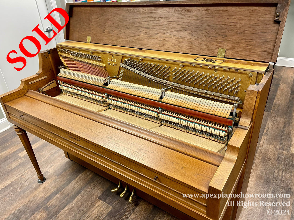An open upright Everett piano with visible hammers and strings, wooden casing, and pedal lyre on a laminate floor in a showroom setting.