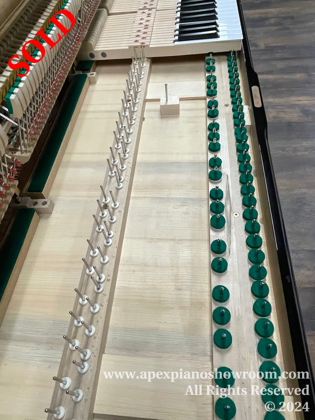 Interior view of an upright piano with hammers, dampers, and strings visible, awaiting maintenance or tuning, in a showroom setting.