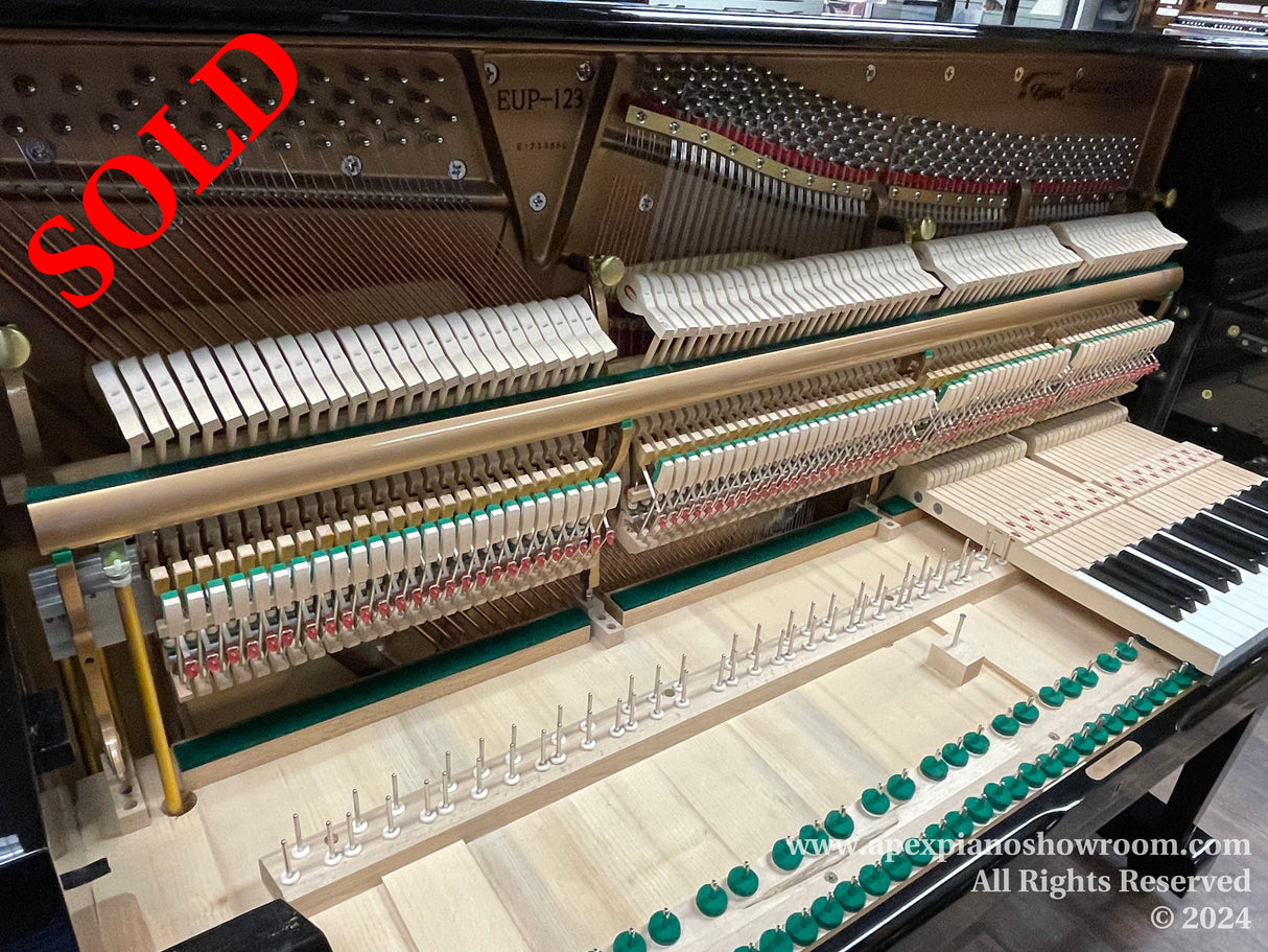 Interior of an upright piano showing hammers, strings, and the action mechanism, with keys partially visible, likely during tuning or maintenance.