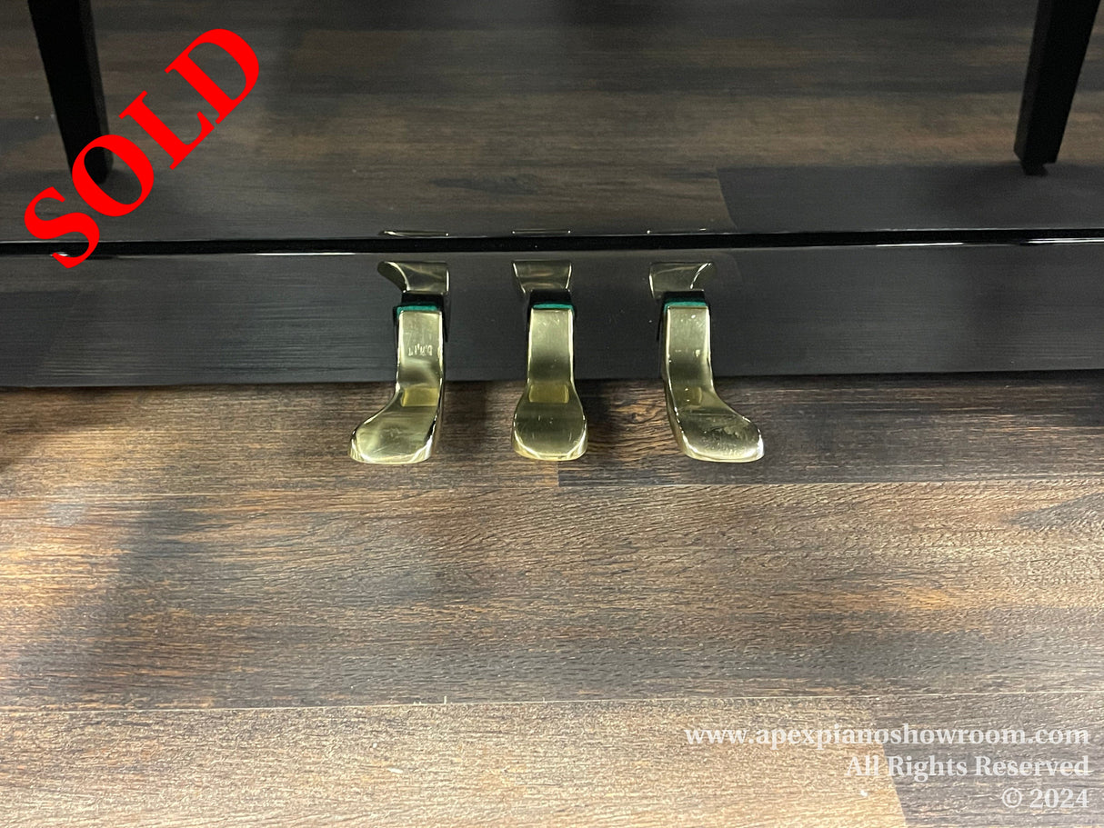 Close-up view of a grand piano's brass pedals, showcasing their polished finish, resting on a wooden floor, indicative of the fine detailing in piano craftsmanship.