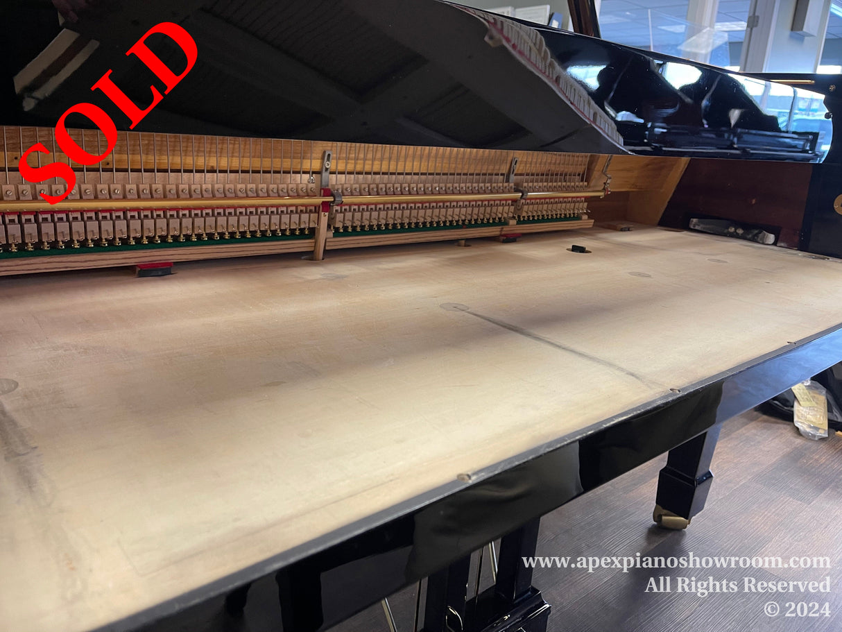 Interior view of a grand piano showing the open instrument with its hammers and strings, situated in a showroom with a reflective black finish on the piano's exterior.