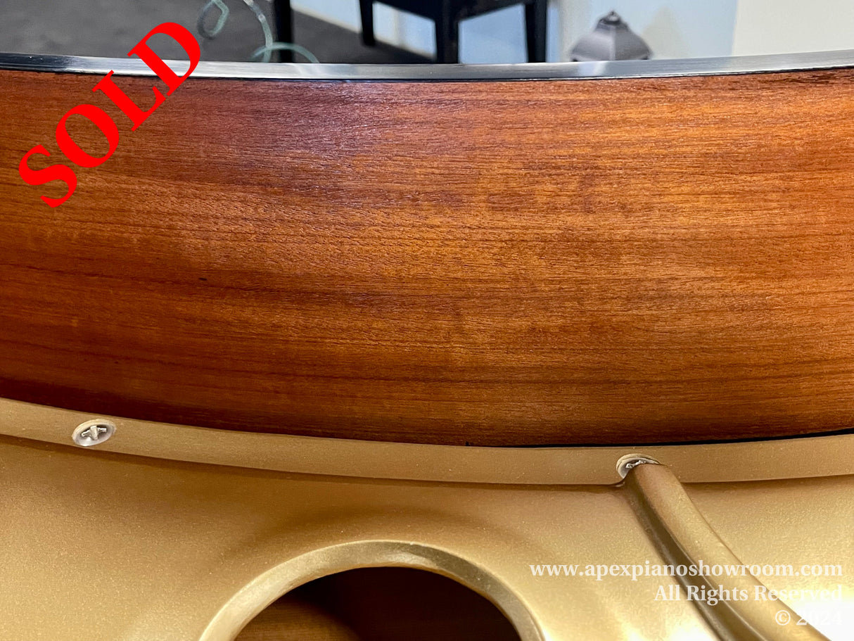 Close-up view of the curve of a grand piano's wood finish and golden frame, showcasing the craftsmanship and quality materials used in piano construction.