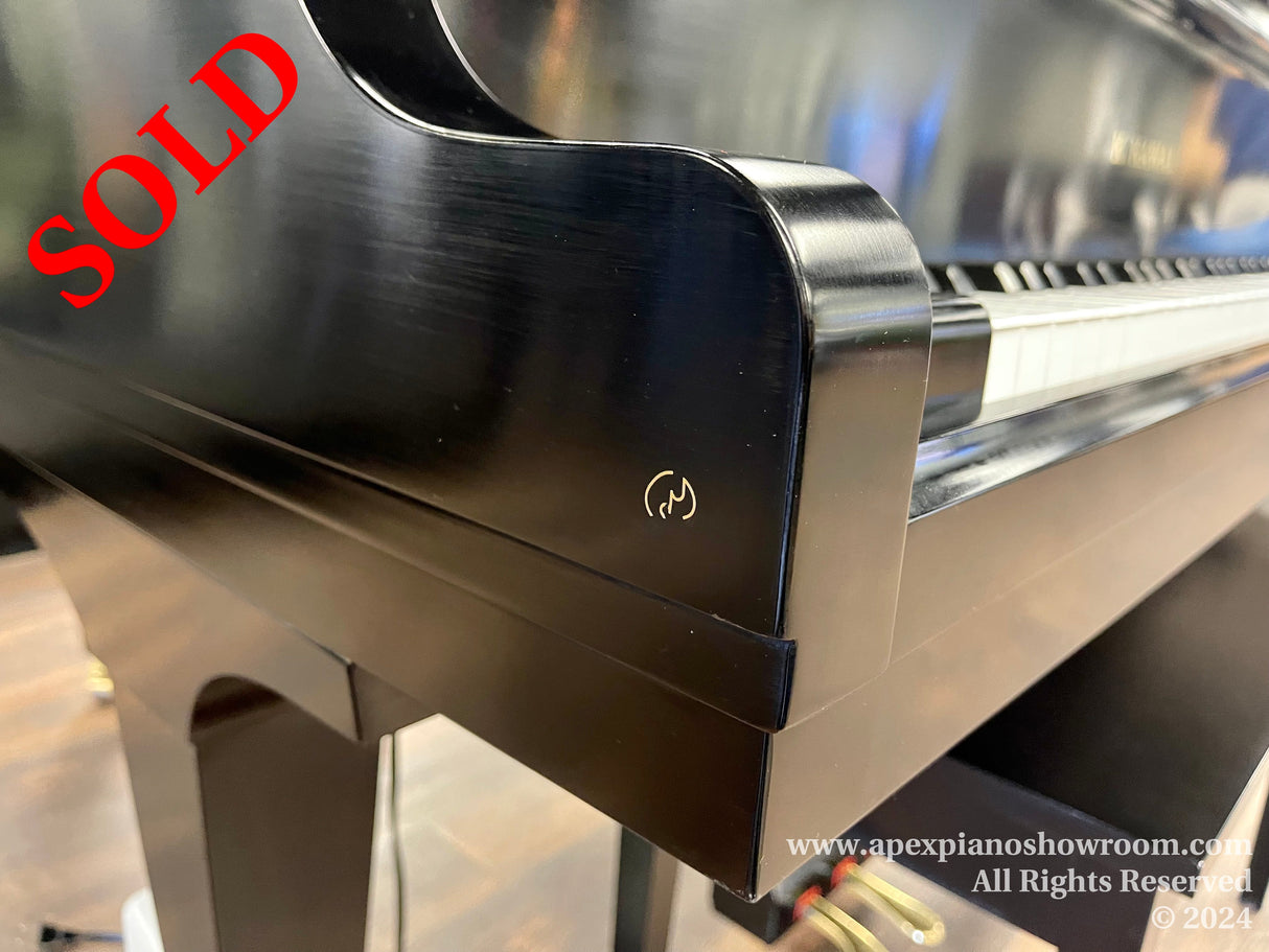 Side view of a black grand piano showcasing its glossy finish and curved leg, with a focus on the elegant silhouette and the manufacturer's logo near the keyboard.