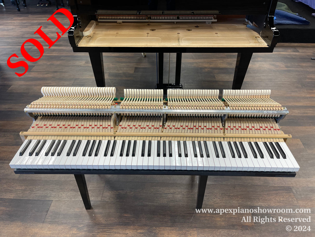 An exposed piano action setup on a stand with keyboard in the foreground, hammer mechanisms visible in tiered rows above keys, and an unfitted dampers section — showcased in a piano showroom with wood flooring, indicating maintenance or educational display.