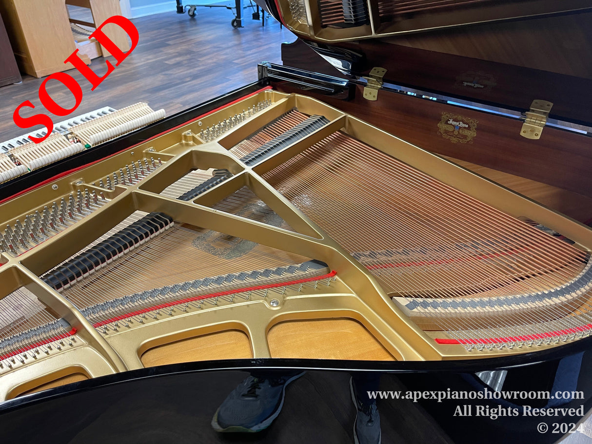 Interior view of a grand piano showing its strings and hammers, with the lid open and the music desk visible, positioned in a showroom with wooden floors.