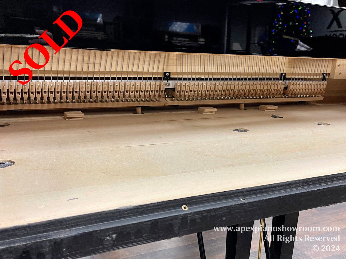 Interior view of a grand piano showing the open mechanism with hammers and strings, indicating a maintenance or tuning process, placed in a piano showroom with a blurred background that includes festive lights.