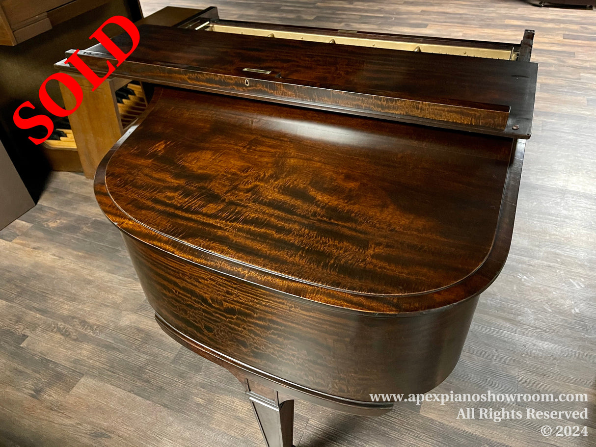 Elegant grand piano with high-gloss wood finish and curved body design, featuring a partially open lid revealing the interior strings and hammers, set against a hardwood floor in a showroom setting.