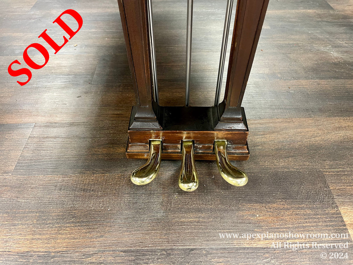 Close-up view of a pianos brown wooden legs on a herringbone patterned floor, with shiny brass casters at the base, indicative of a classic style piano design.