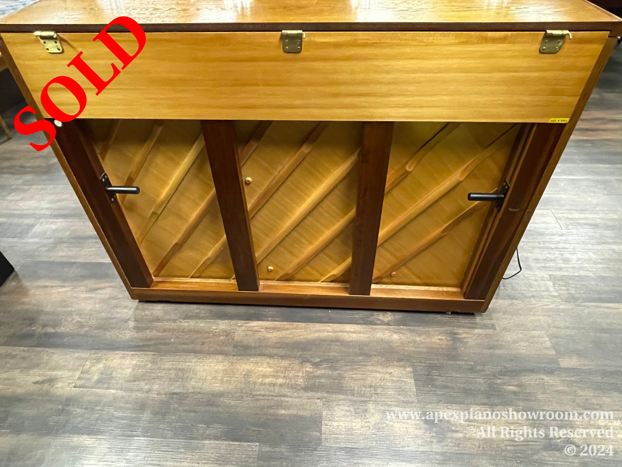 Wooden piano storage cabinet with diagonal shelving for music sheets, shown open with two black handles, on a grey wood-patterned floor.