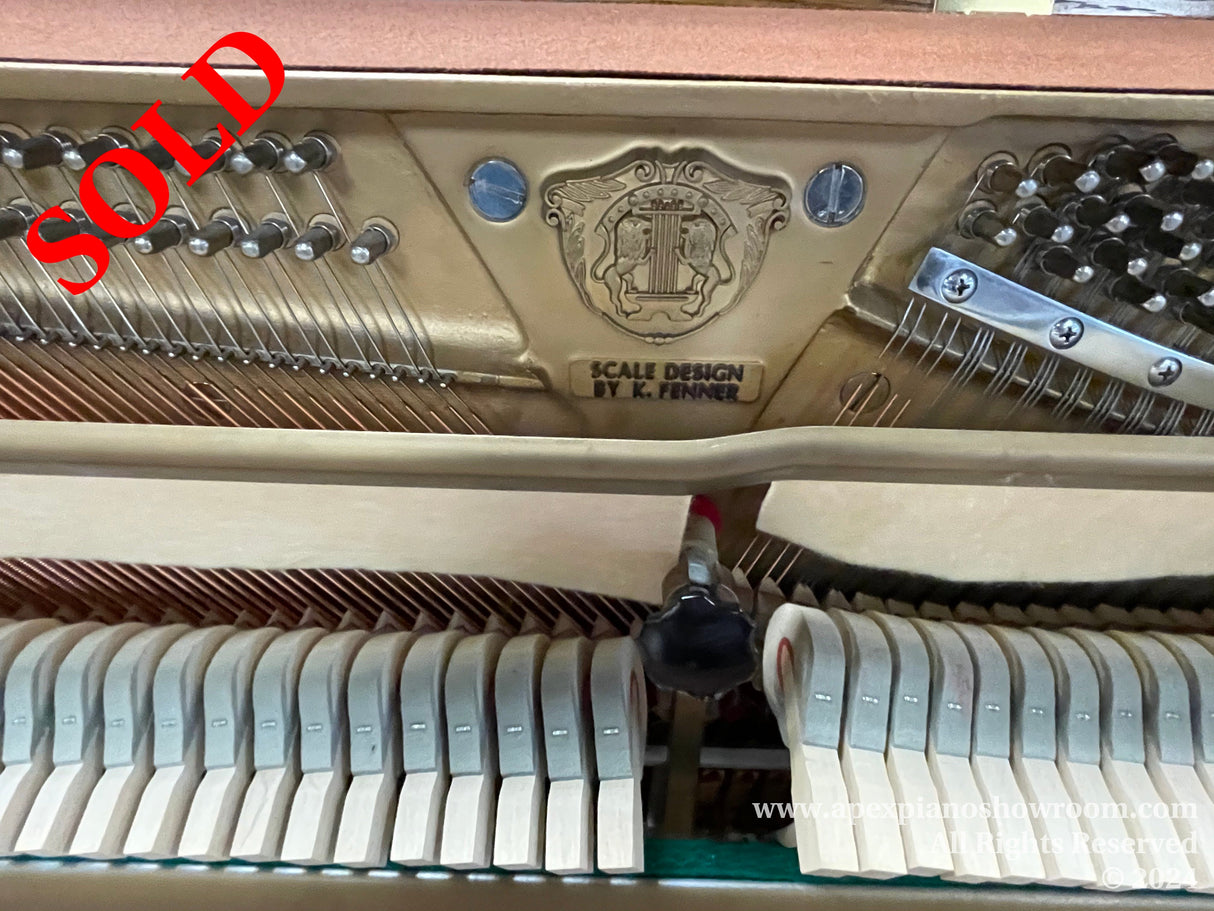 Interior view of a grand piano showcasing the intricate hammer mechanism, strings, and Scale Design by K. Fenner emblem above the keys, with focus on the engineering and craftsmanship involved in piano construction.