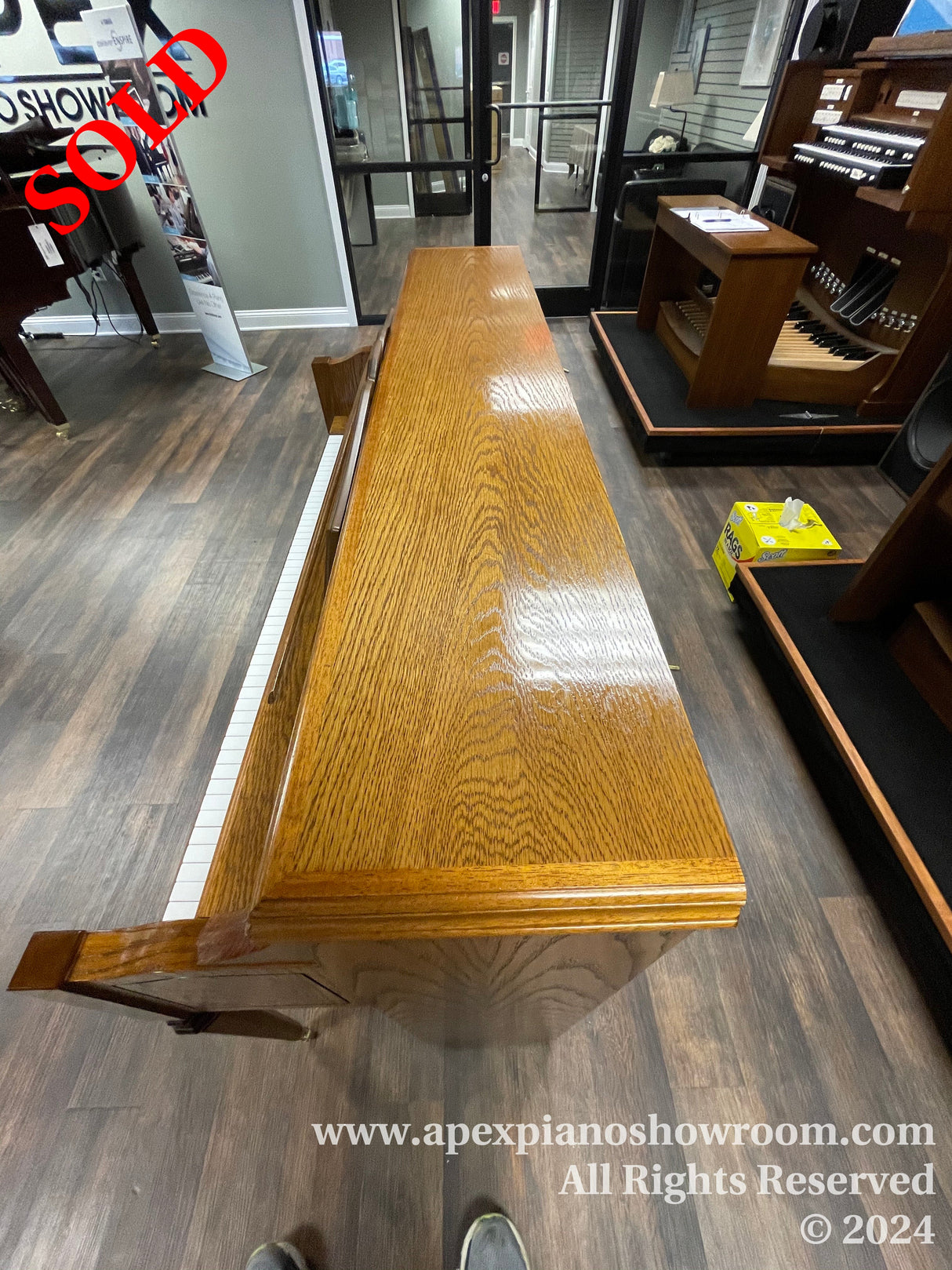 A wooden grand piano in a showroom, showcasing its glossy finish and classic design, with a view of the keyboard and piano bench.
