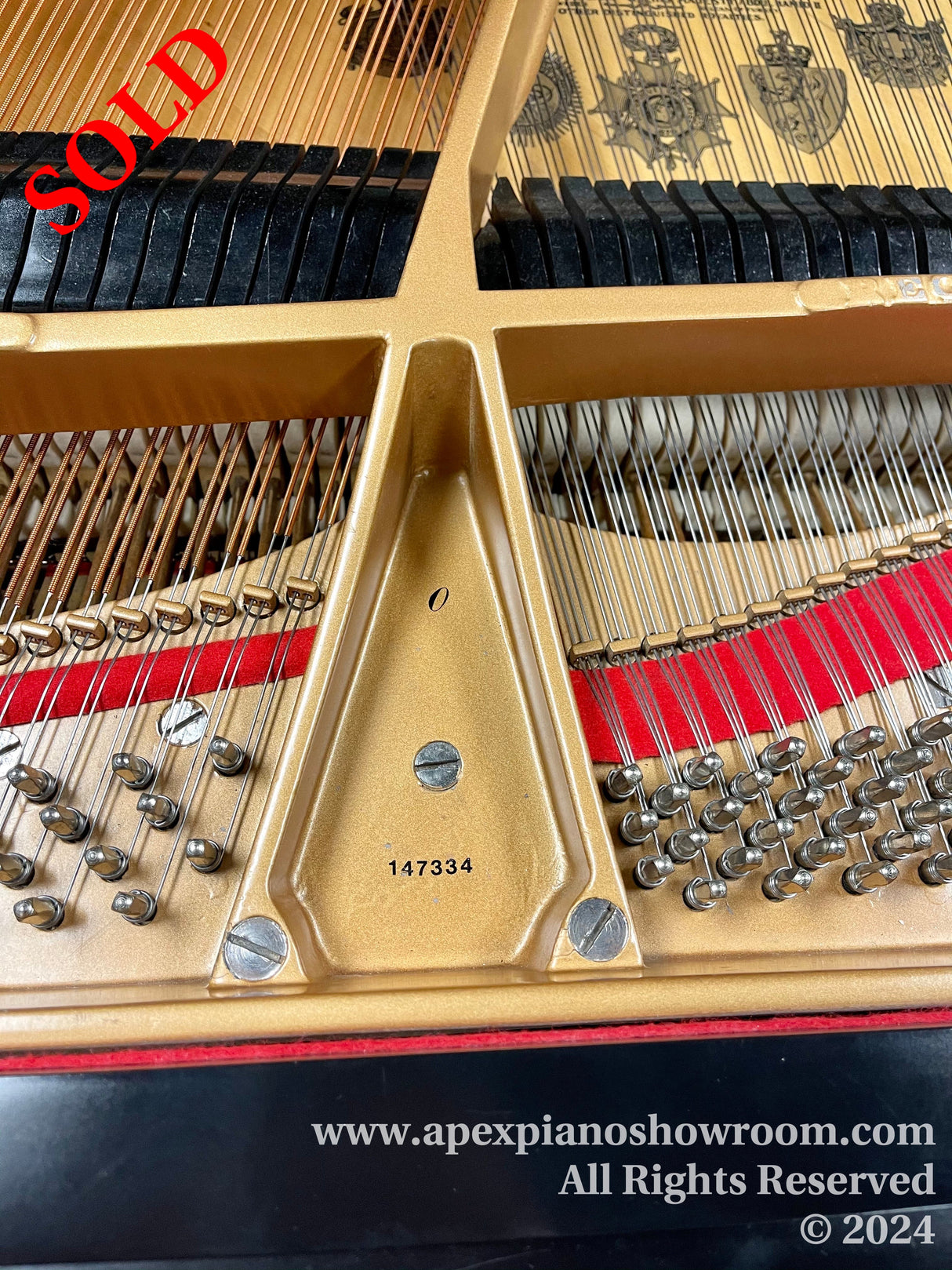 Close-up of a grand pianos gold-painted cast iron plate, showing strings, tuning pins, and dampers, with a visible serial number 147334.