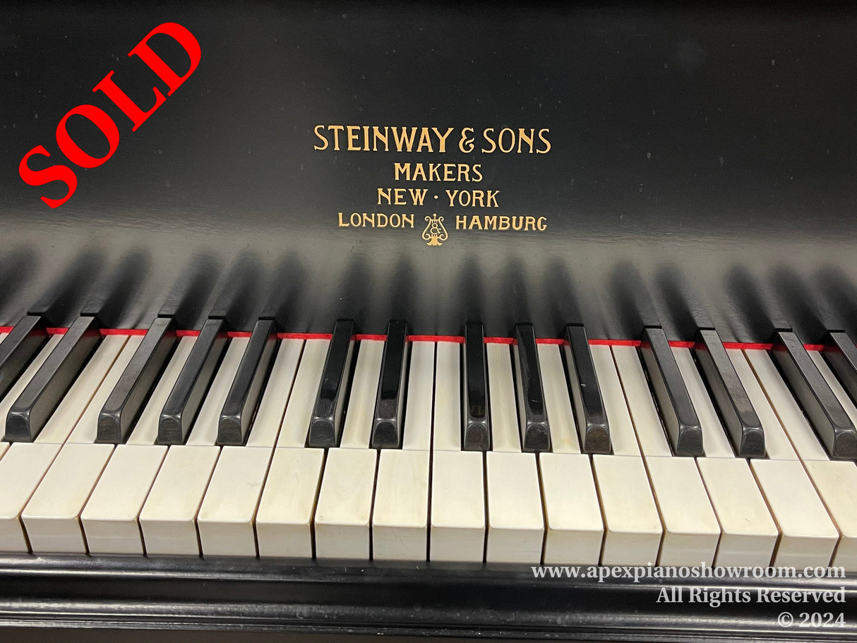 Close-up view of a Steinway & Sons piano keyboard with black and white keys, featuring the Steinway logo above the keys indicating craftsmanship from New York, London, and Hamburg.