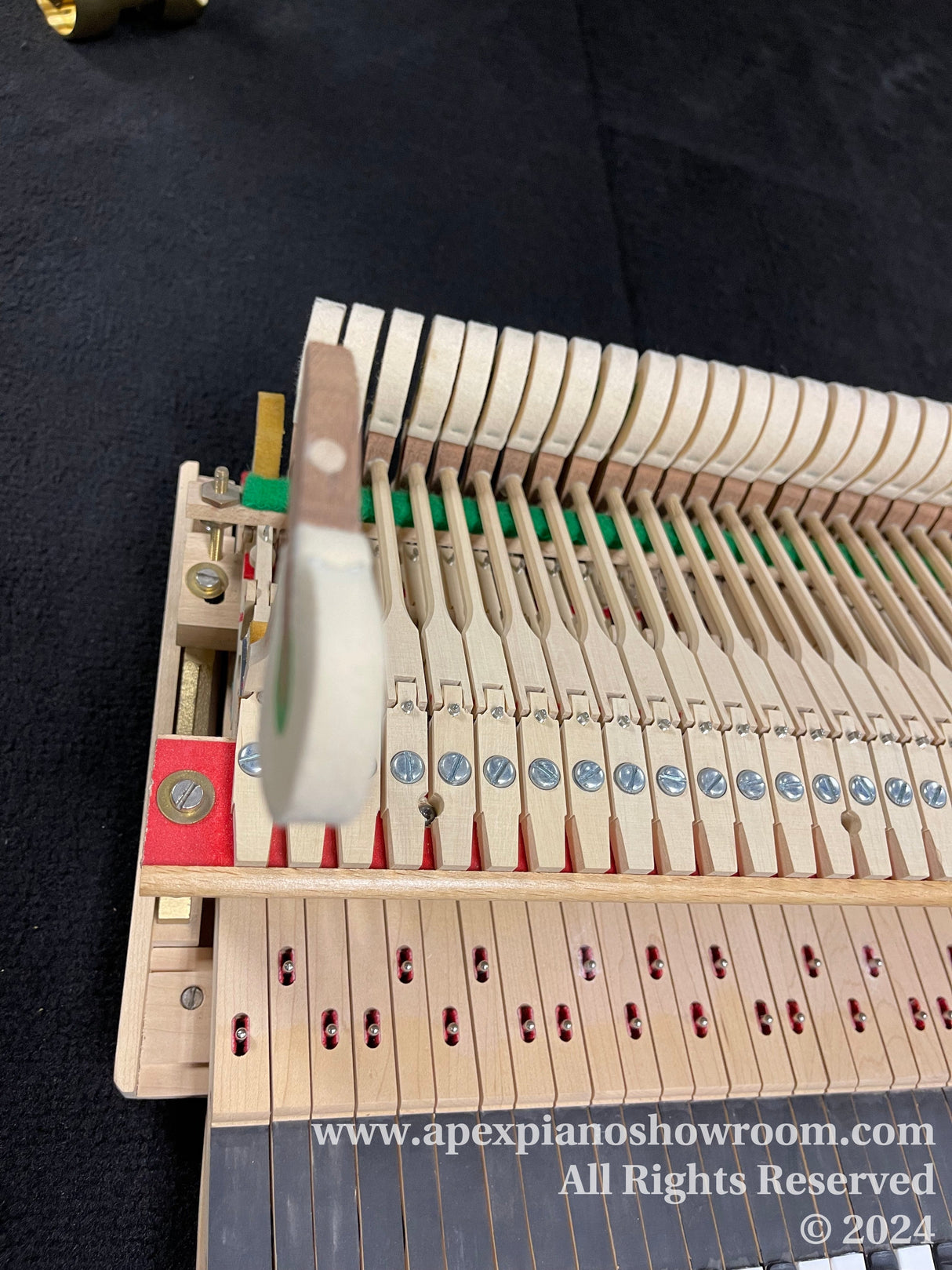 Close-up view of a piano action mechanism from a grand piano, showing hammers, dampers, and strings, with a focus on the regulation and alignment of the parts, on a dark carpeted floor at a piano showroom.