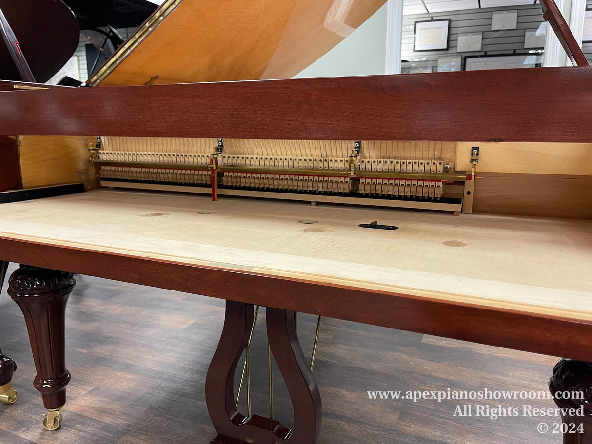 Grand piano with mahogany finish and exposed internal mechanism, showing hammers and strings, set on a showroom floor.