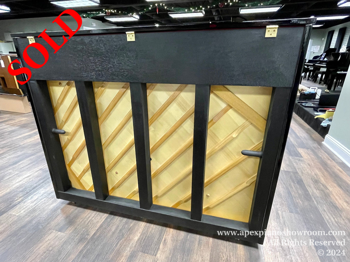 Black upright piano with a unique diagonal wooden lattice music rack design, displayed in a showroom with hardwood floors.