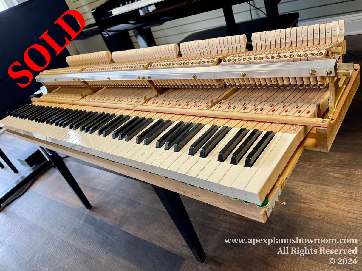 A disassembled grand piano action on a bench with hammers, dampers, and keys visible, set in a piano showroom.
