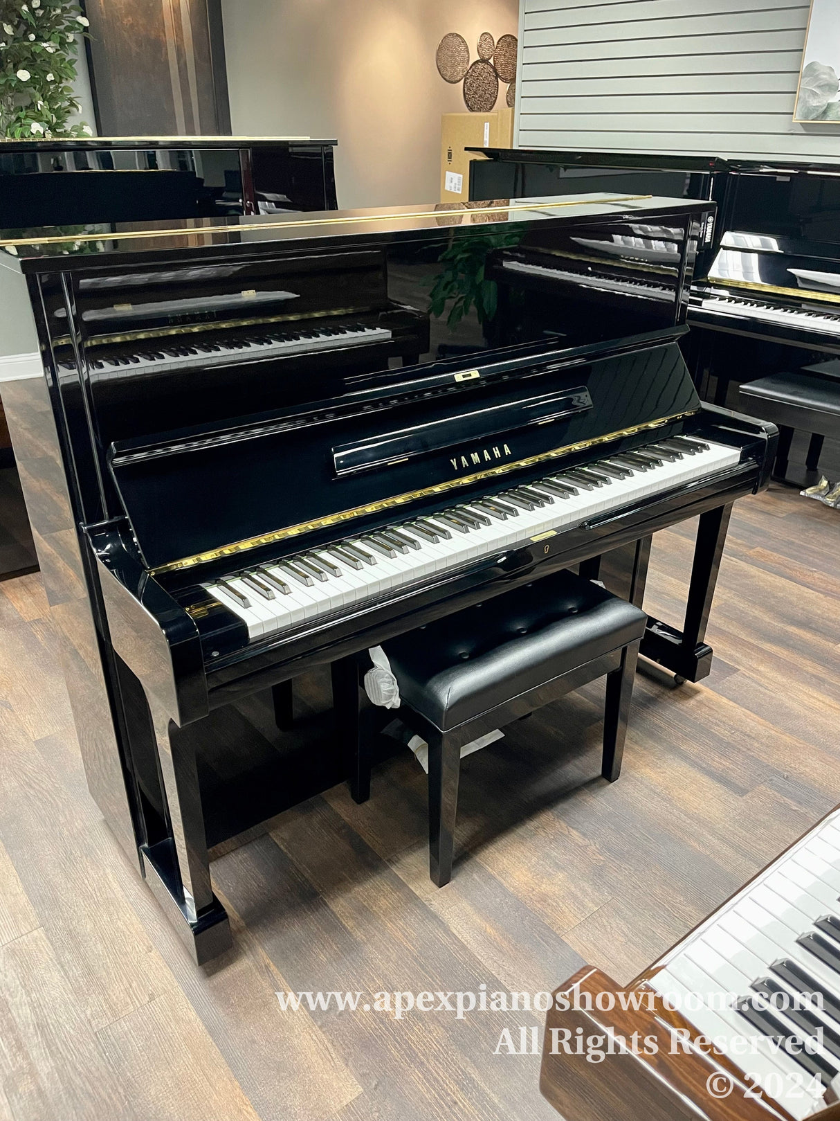 Upright Yamaha piano in showroom with matching bench, polished black finish, reflecting showroom lights.
