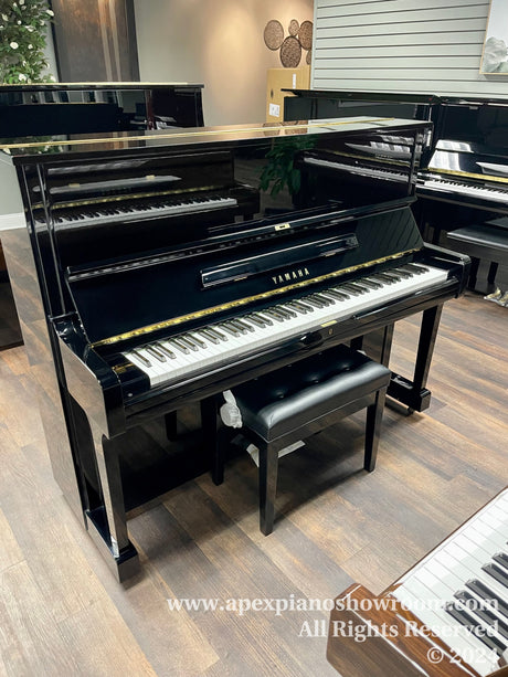 Upright Yamaha piano in showroom with matching bench, polished black finish, reflecting showroom lights.