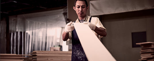 Craftsman inspecting a piece of wood for piano manufacturing in a workshop.