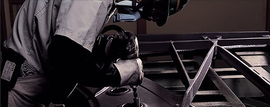 Worker welding metal components for piano frame construction.