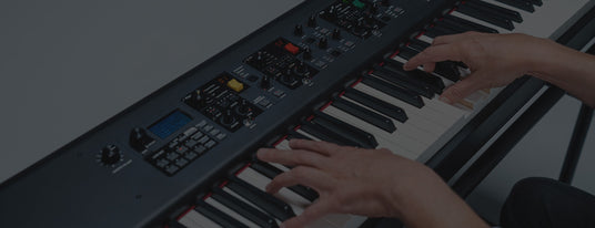Close-up of a musician's hands playing a modern digital piano with various control knobs and an LCD screen, illustrating advanced features for music production in the piano industry.