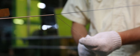Person in a piano manufacturing workshop wearing protective gloves while stringing a piano wire.