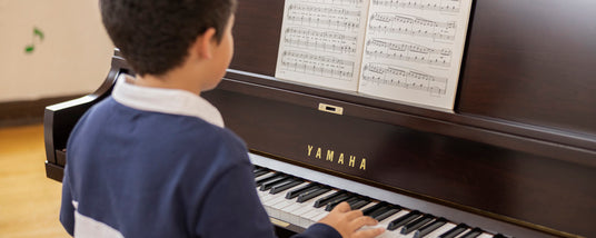 Young pianist practicing on a Yamaha upright piano with sheet music displayed.
