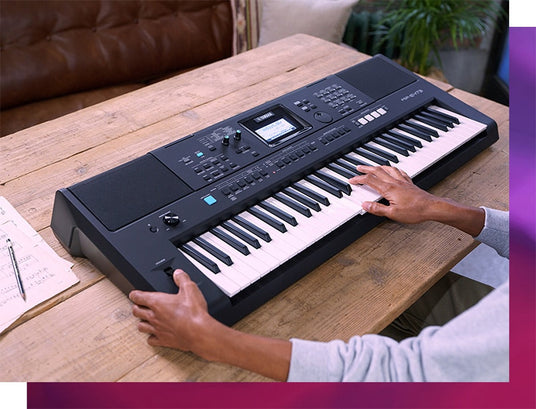 A person playing an electronic keyboard with music scores on a wooden table, indicative of a contemporary pianist's practice session.