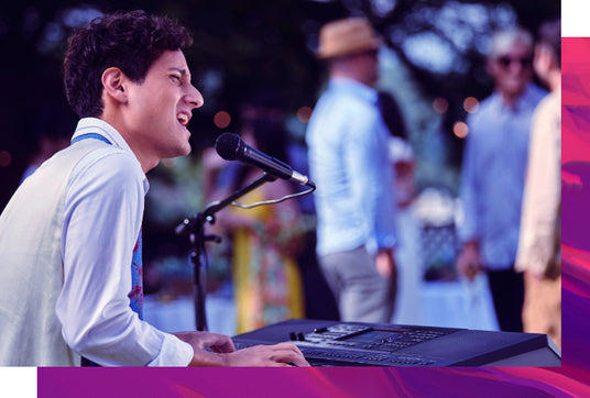 Musician performing at an outdoor event on a digital piano with an audience in the background.