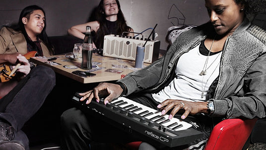 A musician playing a compact digital piano with others playing guitar and enjoying music in a casual setting.