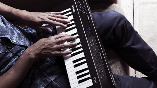 Two individuals playing a duet on a digital piano with visible control panel and brand marking.