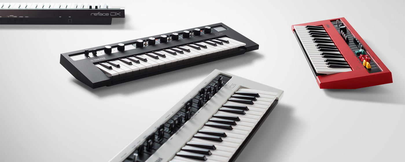 Three modern digital synthesizers on a white surface, showcasing an array of keyboard designs and controls for music production, including a black reface DX model to the left, a white synthesizer with black keys in the middle, and a red synthesizer with pitch bend and modulation wheels on the right.