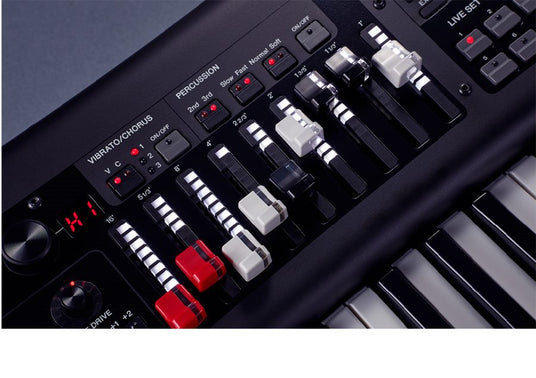 Close-up view of electronic keyboard controls, featuring vibrato/chorus and percussion dials, drawbars, and a section of black and white keys.