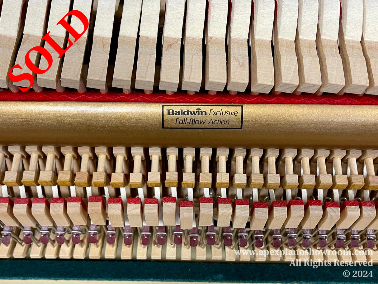 Close-up of a Baldwin pianos internal mechanism featuring the hammer and damper action, with the Baldwin Exclusive Full-Blow Action label visible, showcasing the intricate design and craftsmanship of piano components.