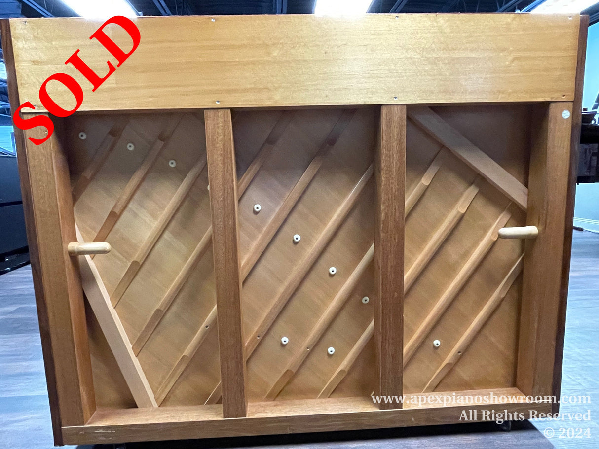 Wooden piano soundboard with diagonal braces visible, indicating the interior structural component of a piano designed for sound quality and durability.