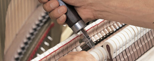 A piano technician tuning a piano by adjusting the tension of the strings using a tuning lever.