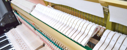 Close-up view of the internal mechanism of a grand piano, showing hammers, strings, and dampers.